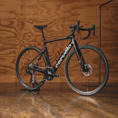 A Glossy Black Cervelo Caledonia with Shimano 105 Di2 in a plywood room