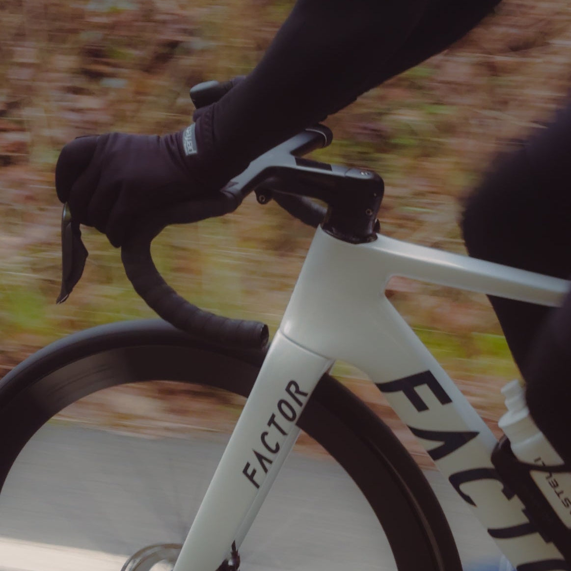 Close-up of a person riding a white bicycle with 'Factor' branding on a blurred natural background.