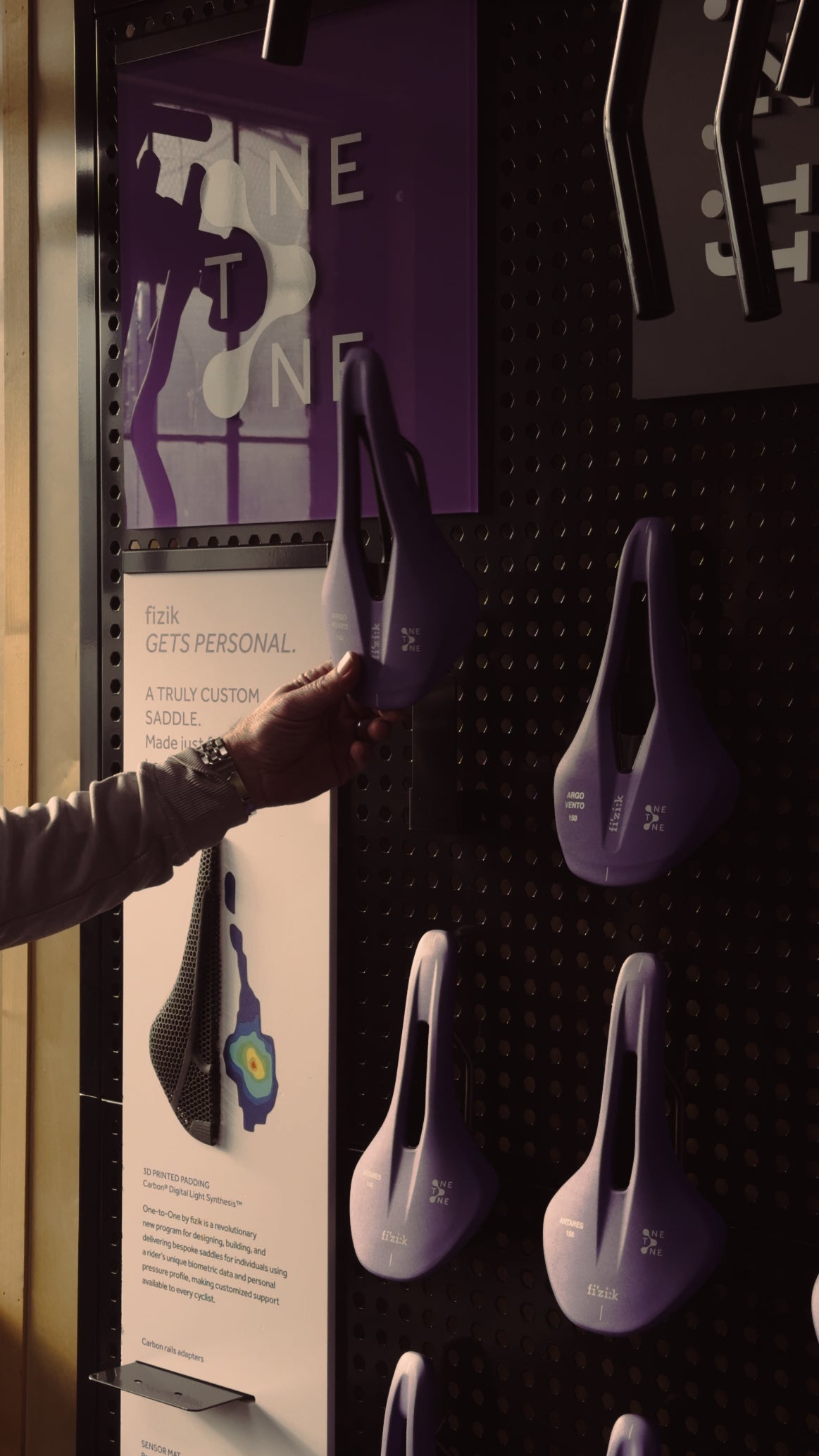 A hand reaching for a 1-to-1 Fizik saddle on a Fizik saddle display