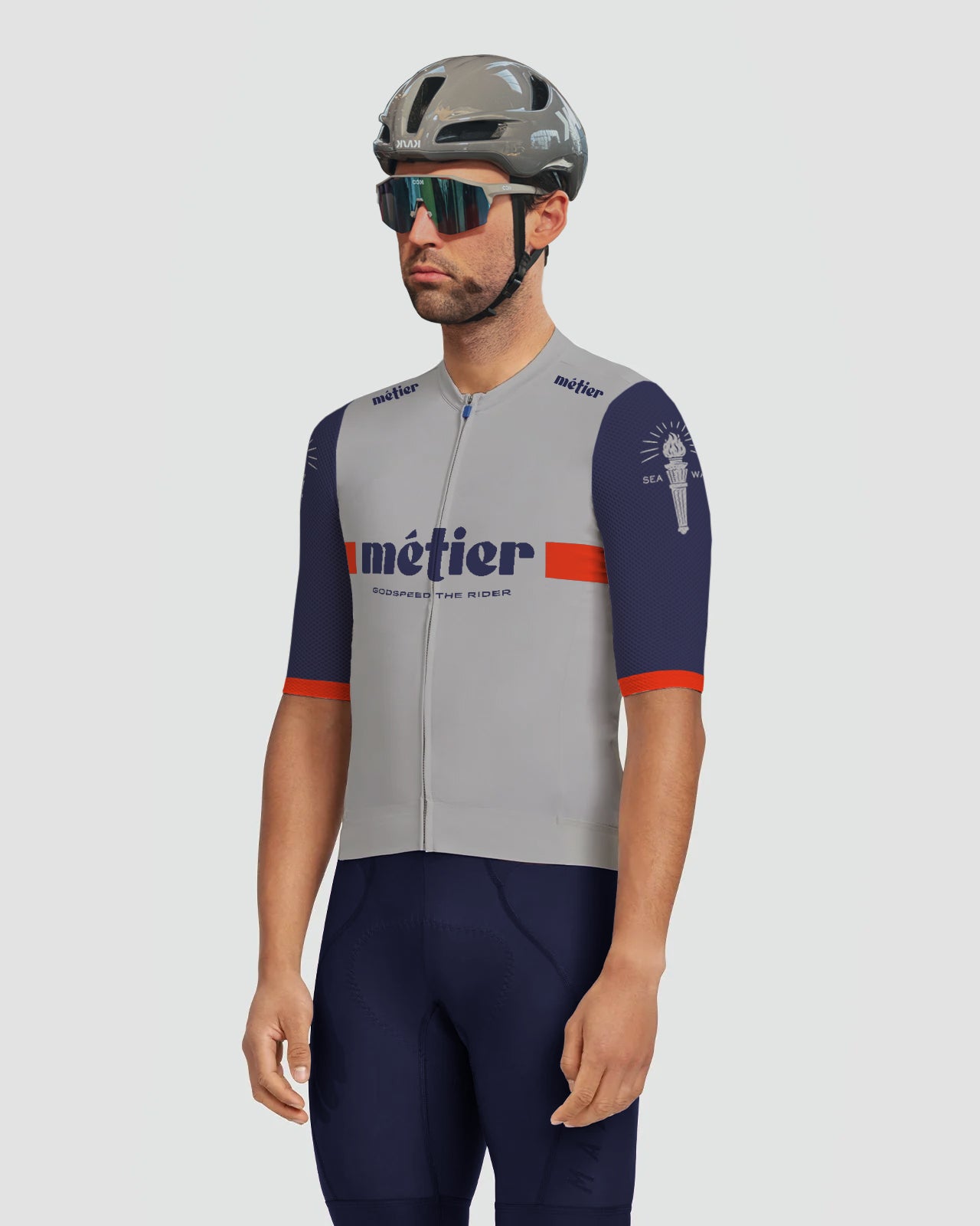 A Metier Riders Club Member wearing a Metier Racing team kit with grey body and navy blue sleeves, and a grey Kask Utopia Helmet