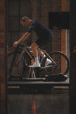 A professional bike fitter at Metier Cycling & Cafe in Seattle checks knee alignment on a road cyclist during the final fit adjustment on their custom bike sizing session.  