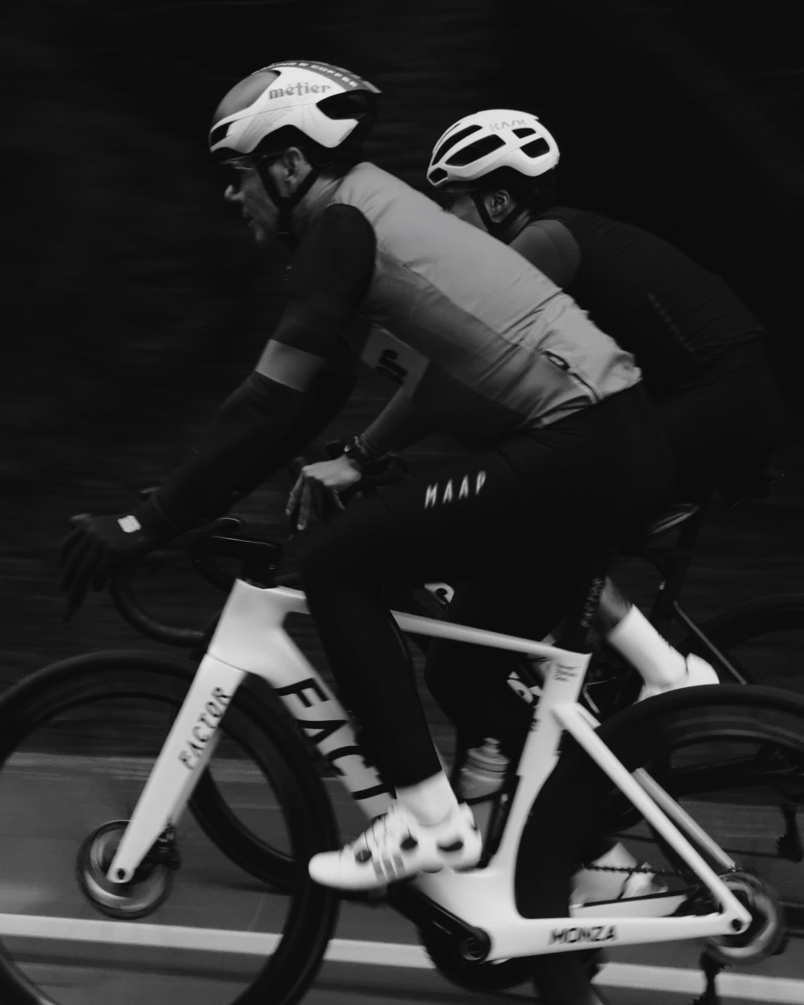 A Black and White image of two Metier Club Cyclists riding their road bikes on a group ride, one riding a Factor Monza.