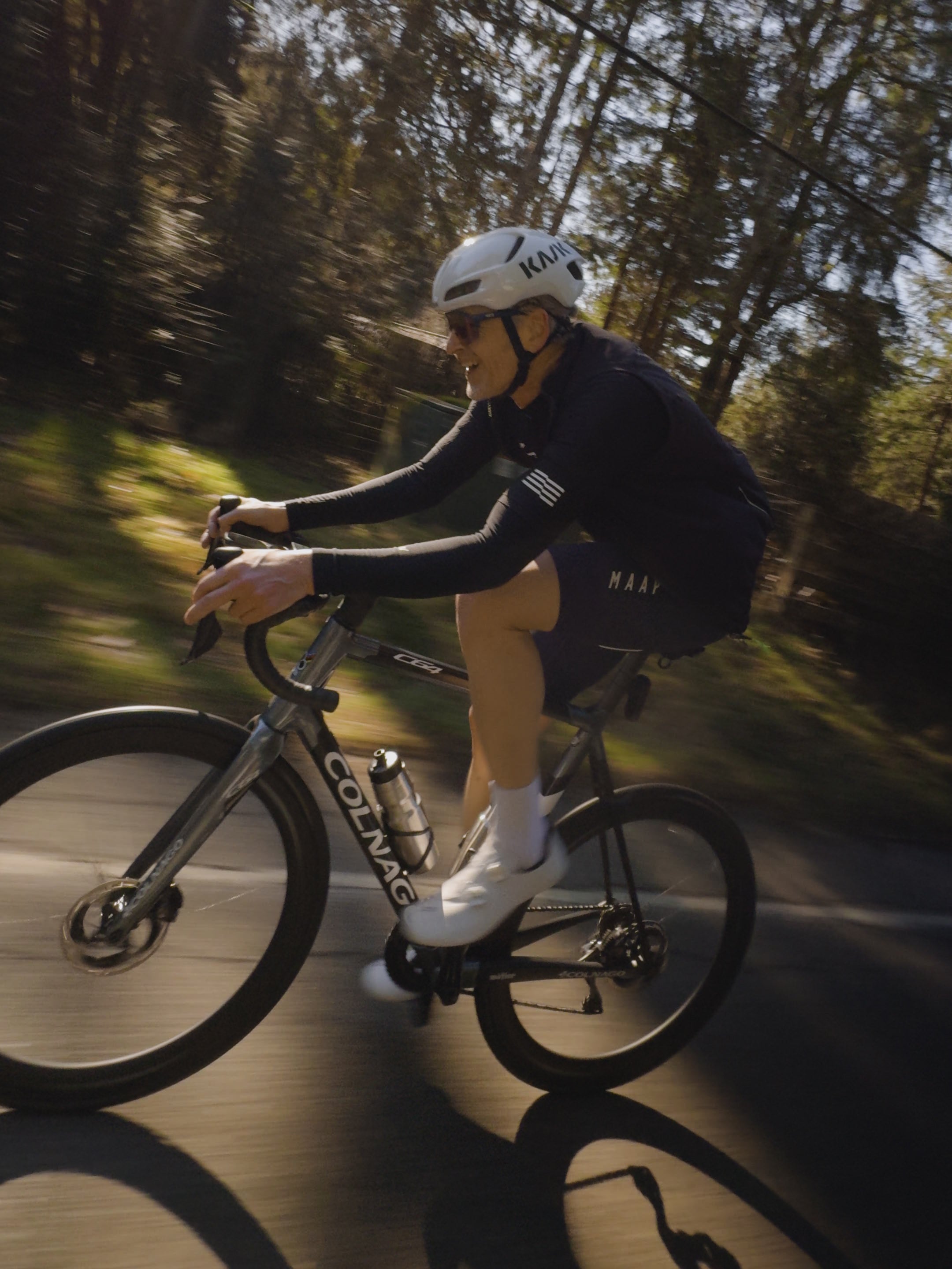 A metier club cyclist riding a Colnago C64 through a patch of sunlight during a seattle group ride.