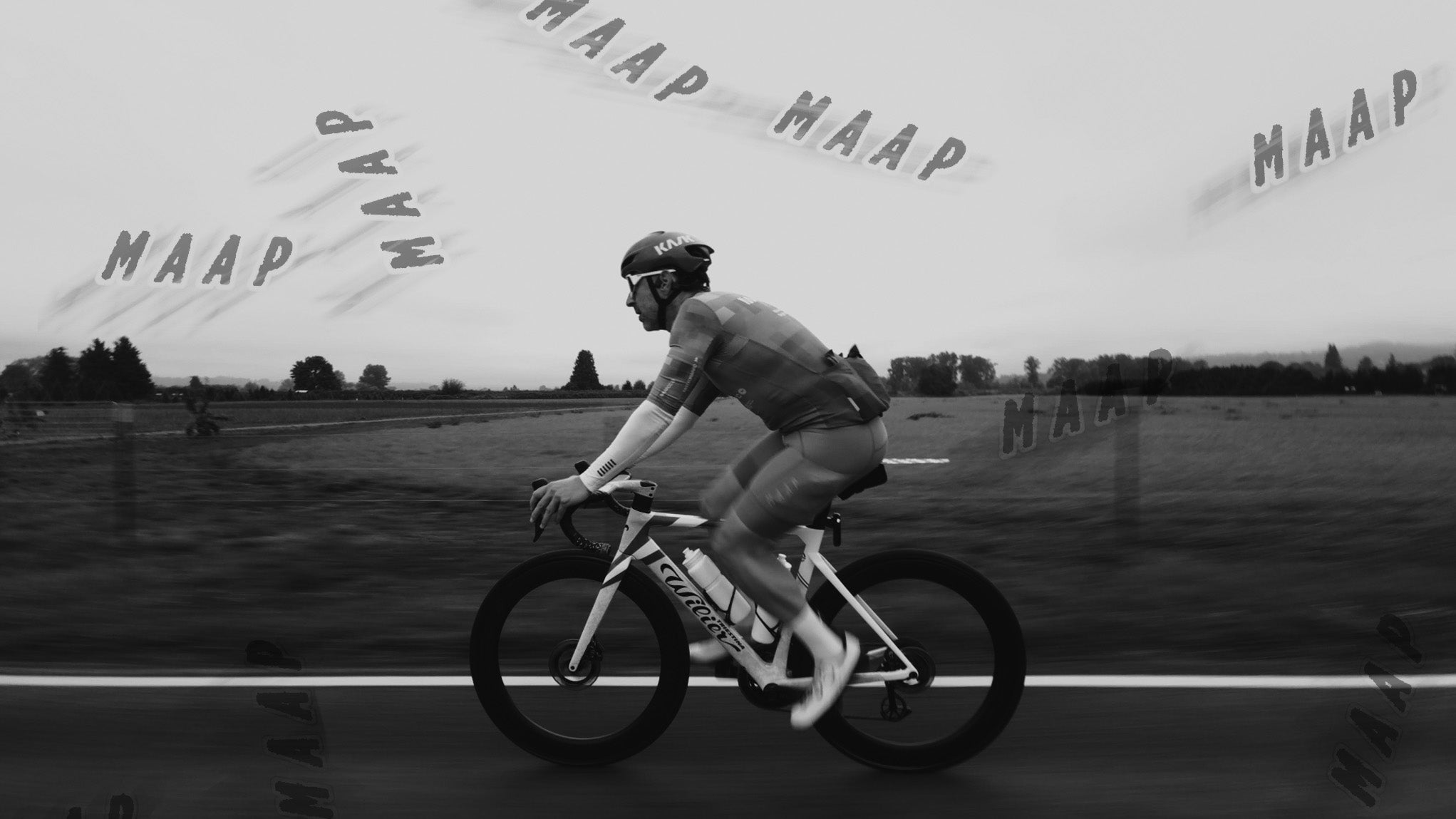 A road cyclist in MAAP kit riding a Wilier Filante down a rural road, with MAAP logos burned in the image background
