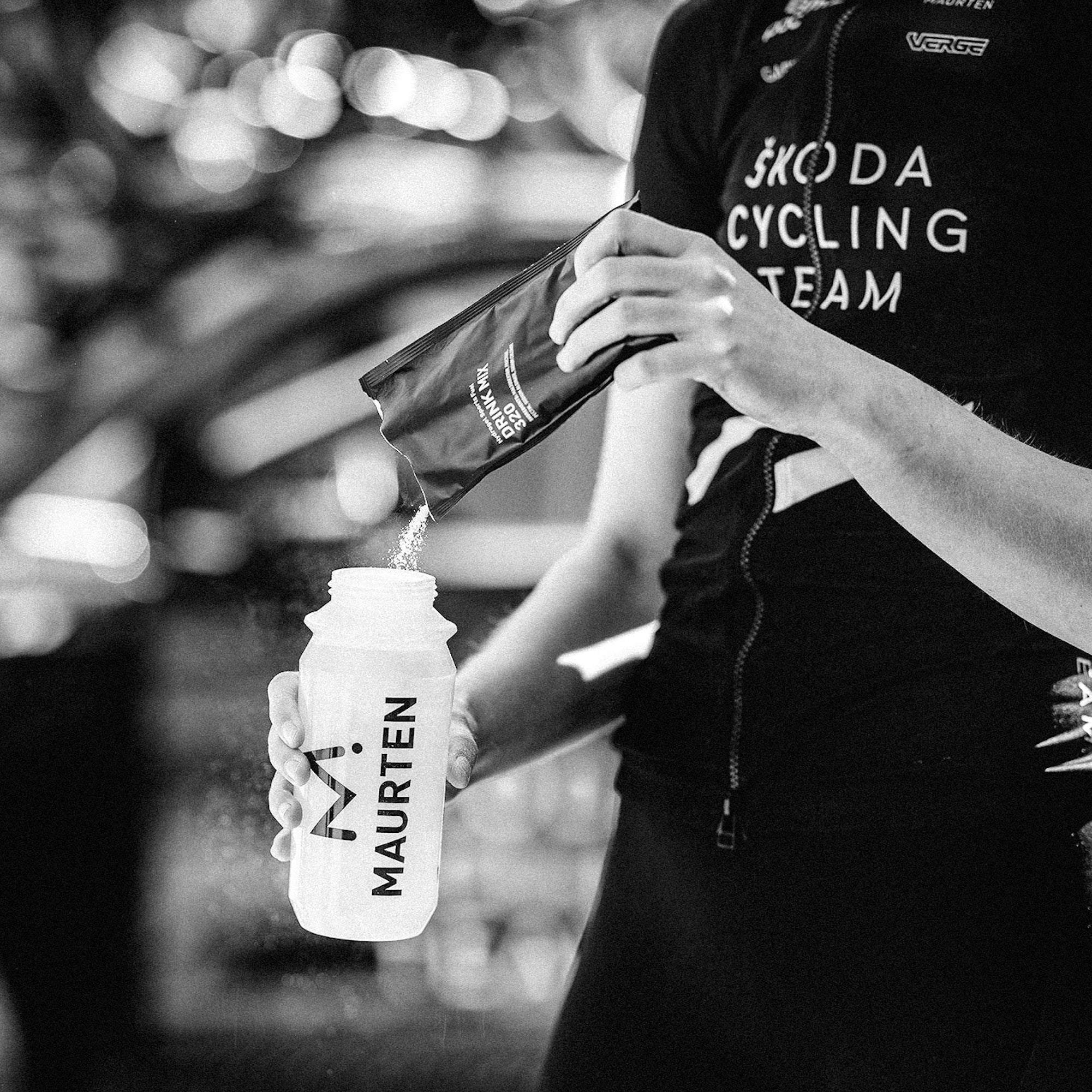 A cyclist pouring Maurten Drink Mix 320 into a Maurten branded-bottle.