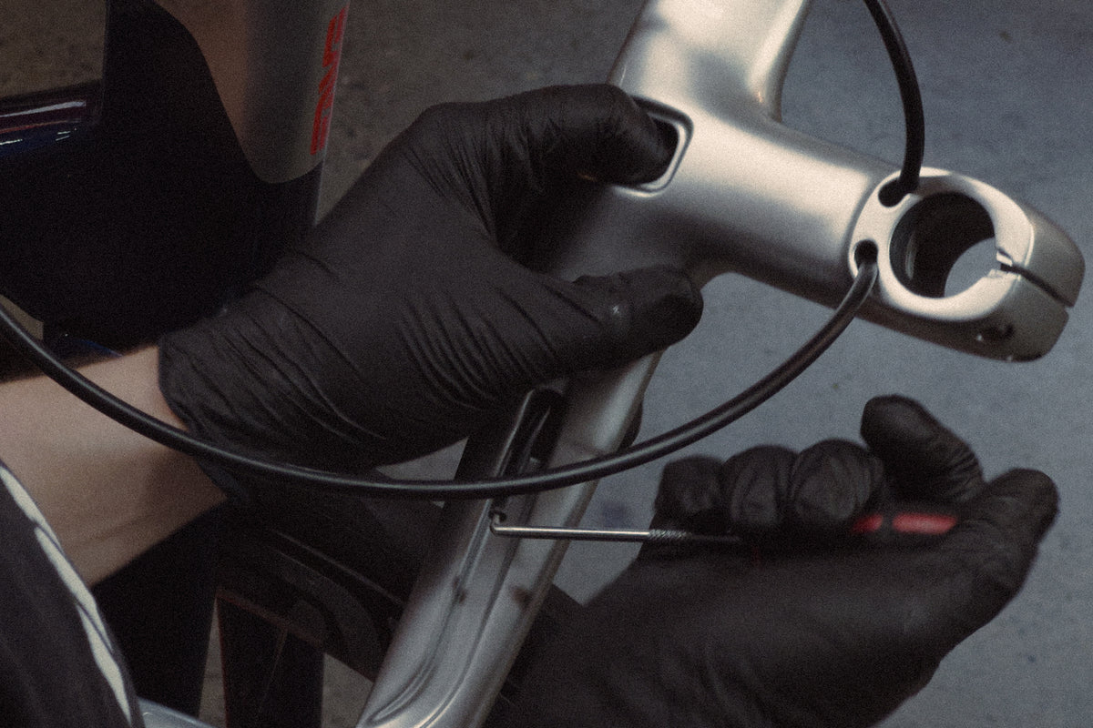 A close up of a bike mechanic feeding a brake hose through and Enve integrated bar stem.
