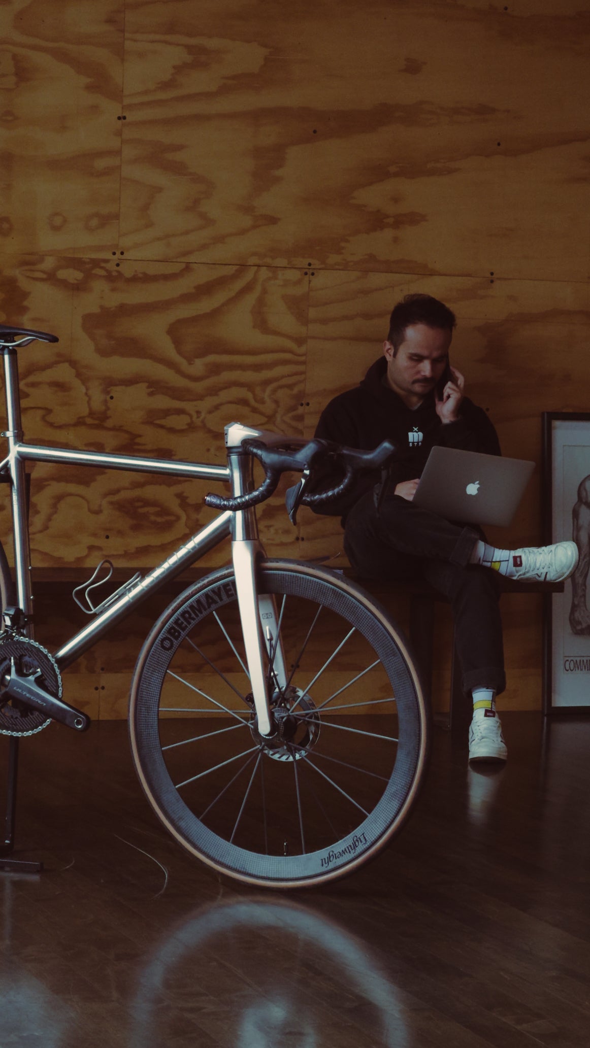 A custom Passoni titanium bike in front of a man sitting on his laptop in a plywood room