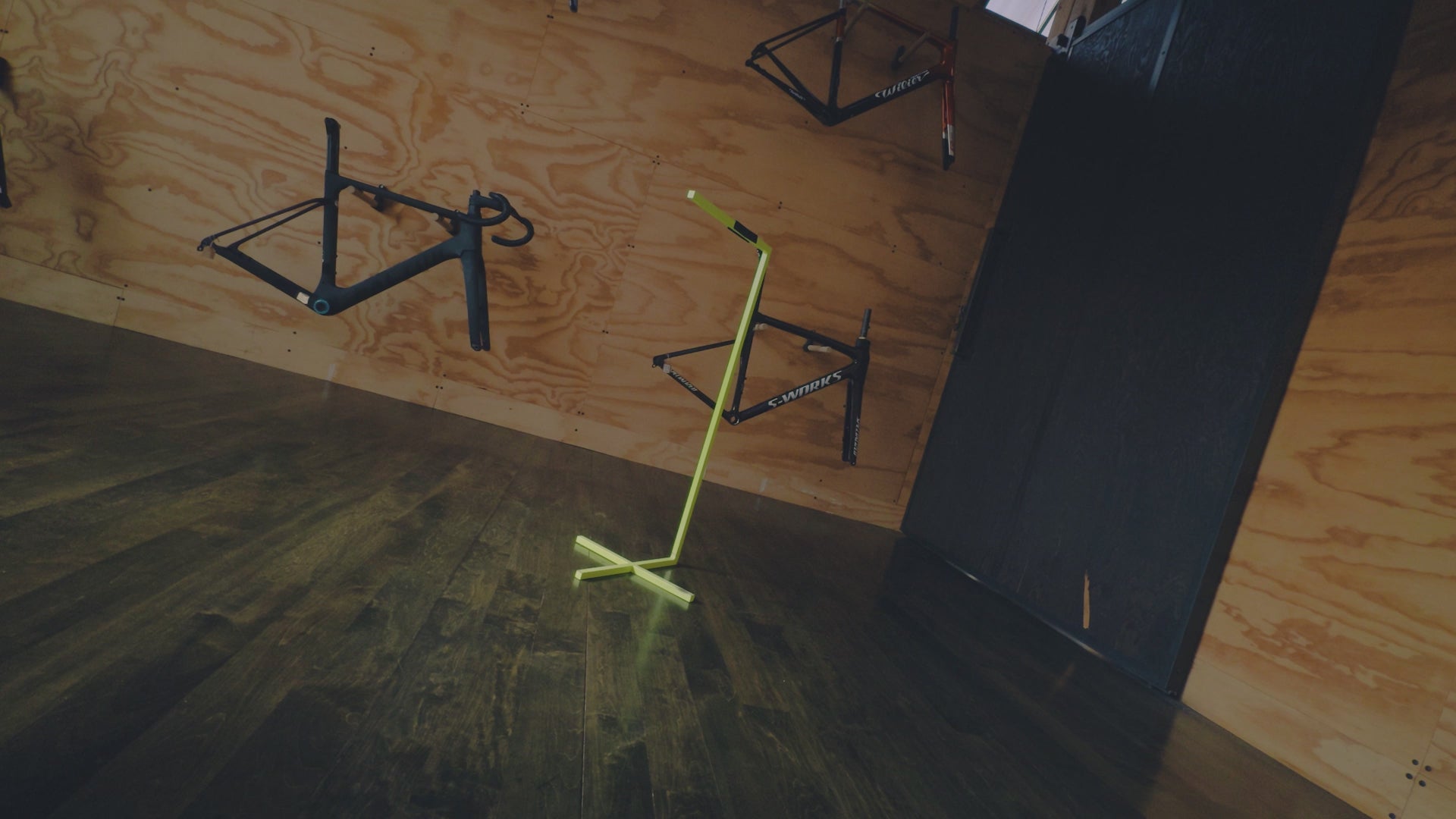 A Five Black Cervelo S5 with SRAM Red AXS groupset and Vision Metron 45 SL wheels being placed on a bike stand in a plywood room.